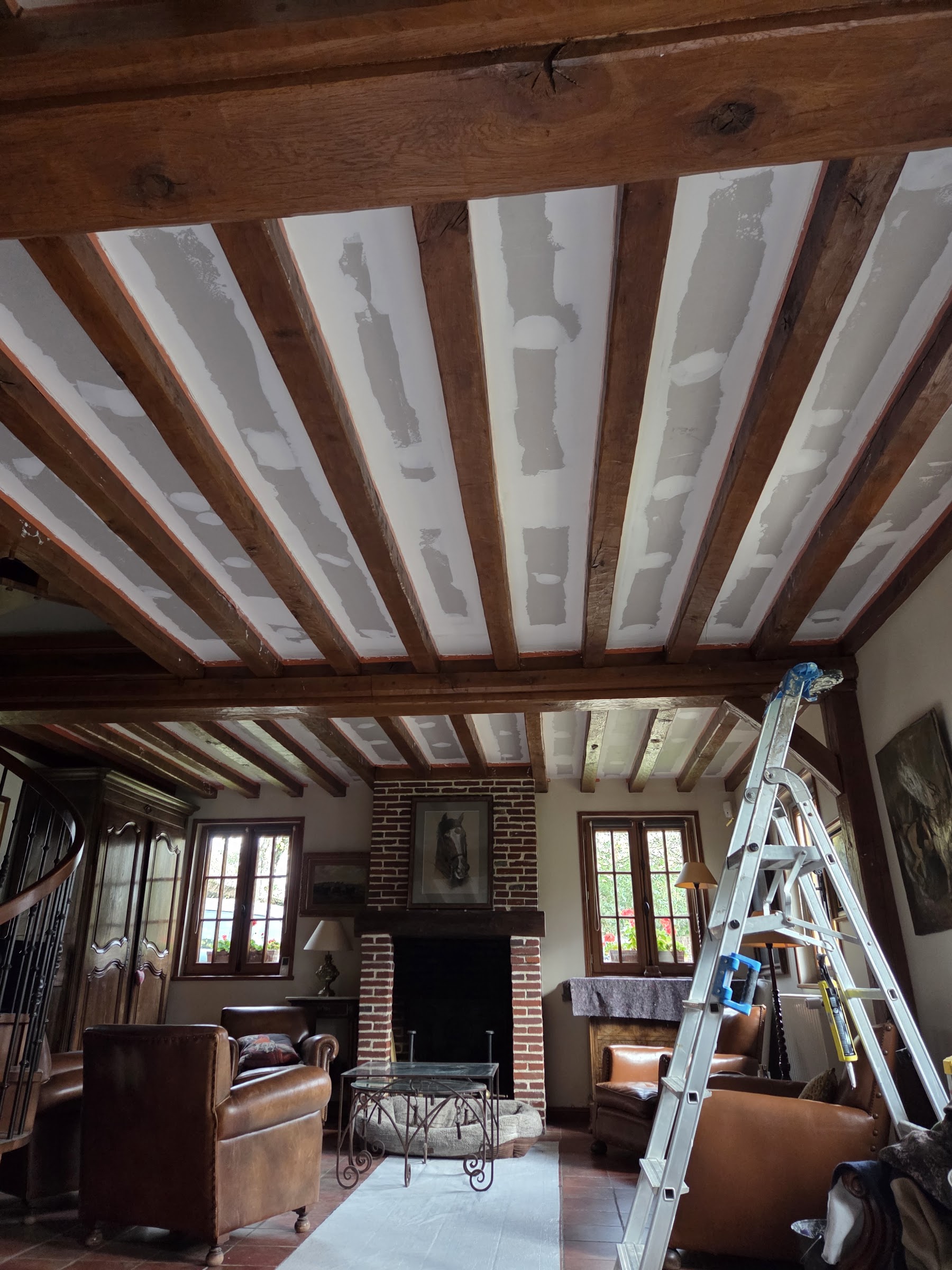 Salon avec poutres apparentes et cheminée en briques dans une maison ancienne